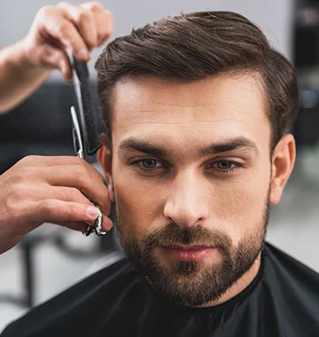 Man with side of hair being styled by barber holding scissors and comb